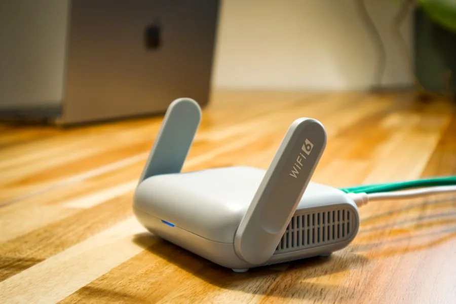 Compact white wireless access point with a green patch lead on a timber desk