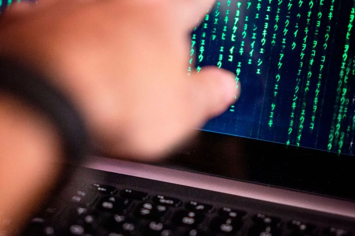 Finger pointing at a screen of scrolling green code, a hacked website