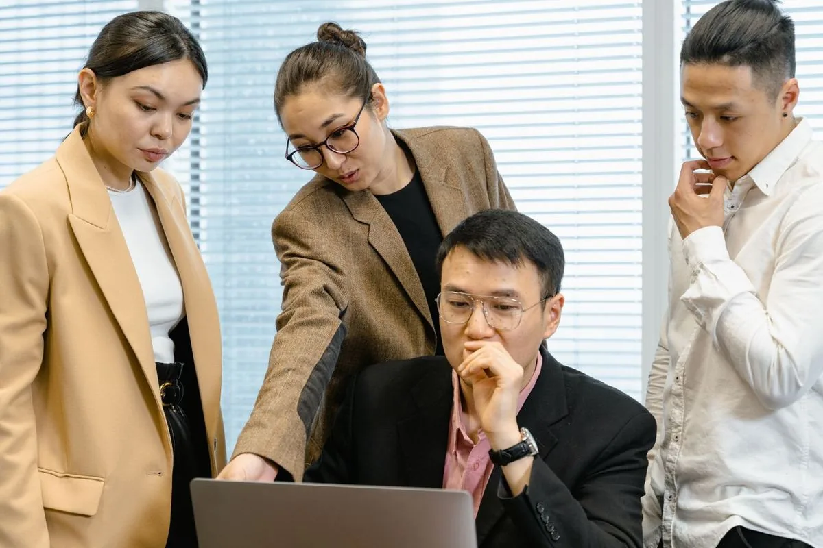Office team gathered behind a manager at his laptop, reviewing a broken database